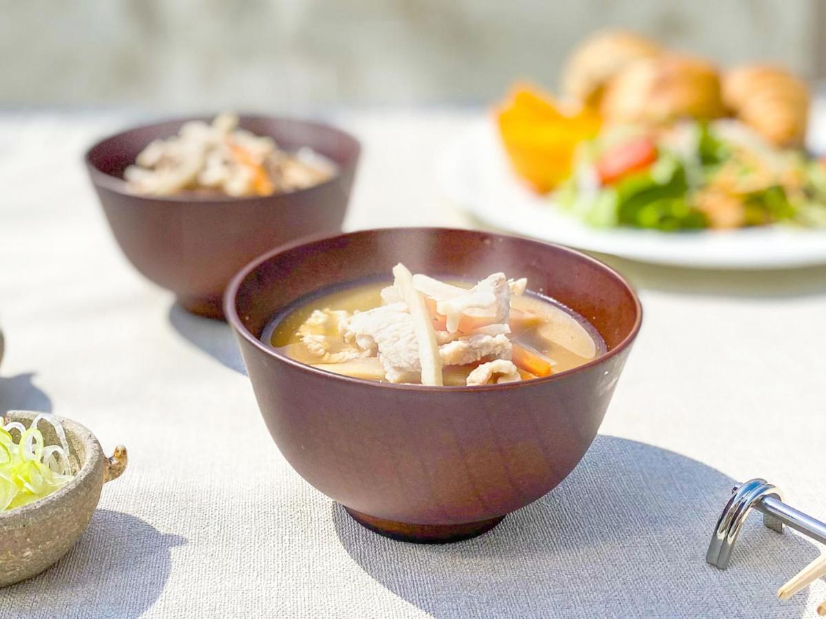 فندق كوبي ميريكين بارك أورينتال كوبه المظهر الخارجي الصورة The photo features a wooden bowl filled with a warm soup containing pieces of meat and vegetables. There are also two additional bowls in the background, along with a plate of salad and baked goods, suggesting a meal setting. The table is covered wit