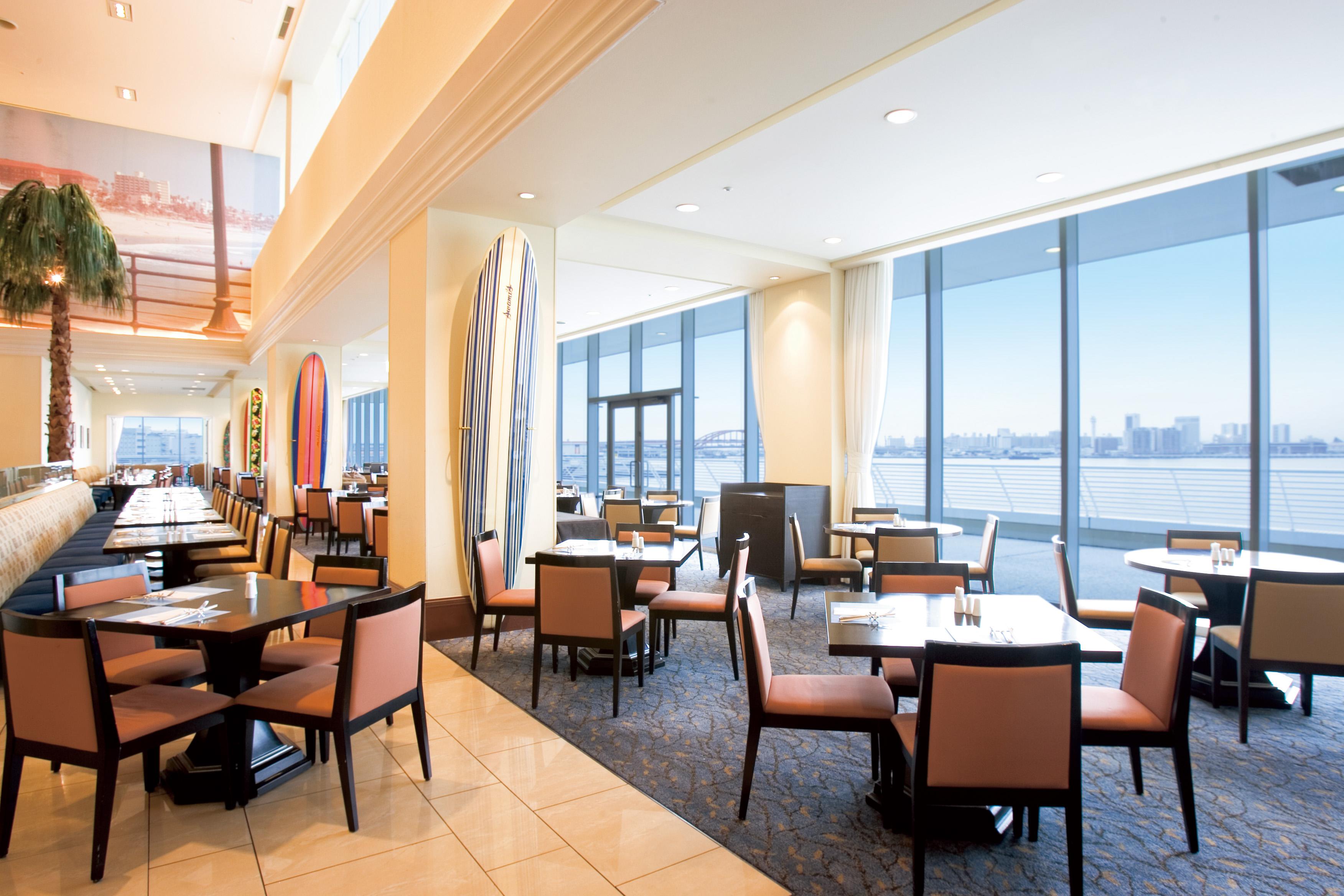 فندق كوبي ميريكين بارك أورينتال كوبه المظهر الخارجي الصورة The photo shows a modern dining area or restaurant with large windows that provide a view of the outside, likely featuring a scenic city or waterfront. The interior design includes tables and chairs arranged throughout the space, with a stylish and c