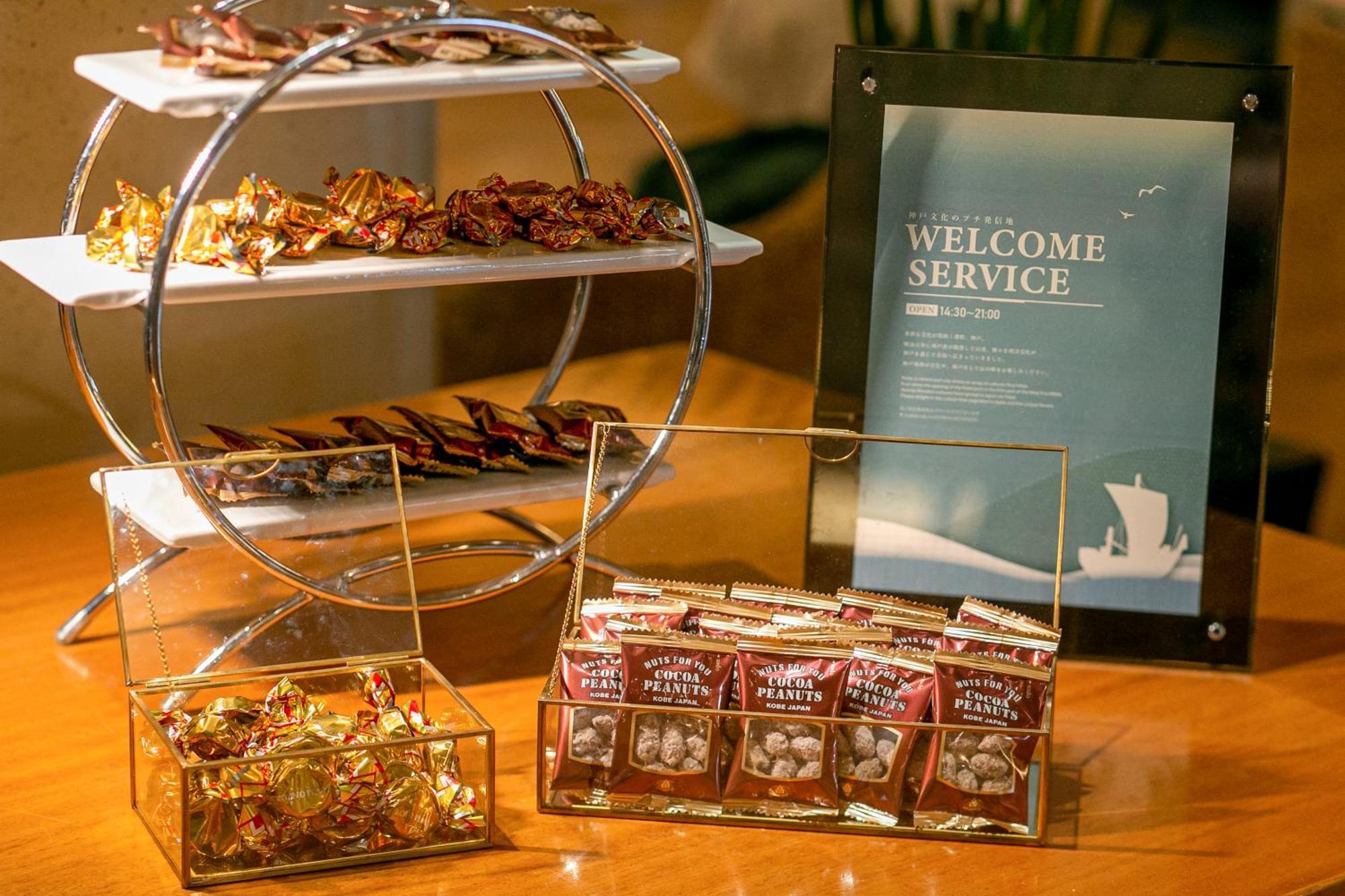 فندق كوبي ميريكين بارك أورينتال كوبه المظهر الخارجي الصورة The photo displays a welcome service setup featuring various treats. 

1. **Display Stand**: There is a tiered circular stand with an assortment of wrapped candies or chocolates on the upper and lower levels.

2. **Glass Container**: In front, there'
