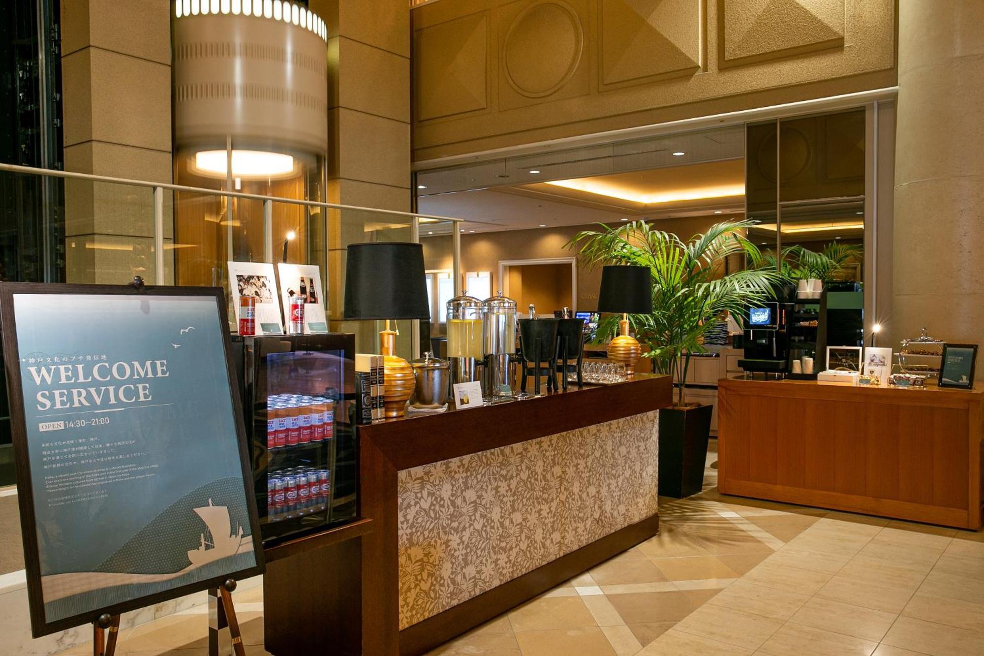 فندق كوبي ميريكين بارك أورينتال كوبه المظهر الخارجي الصورة The photo depicts an elegant reception area, likely in a hotel. There is a large sign that reads "WELCOME SERVICE" positioned prominently on the left. 

The reception desk is well-organized, featuring decorative elements like lamps and a beverage are