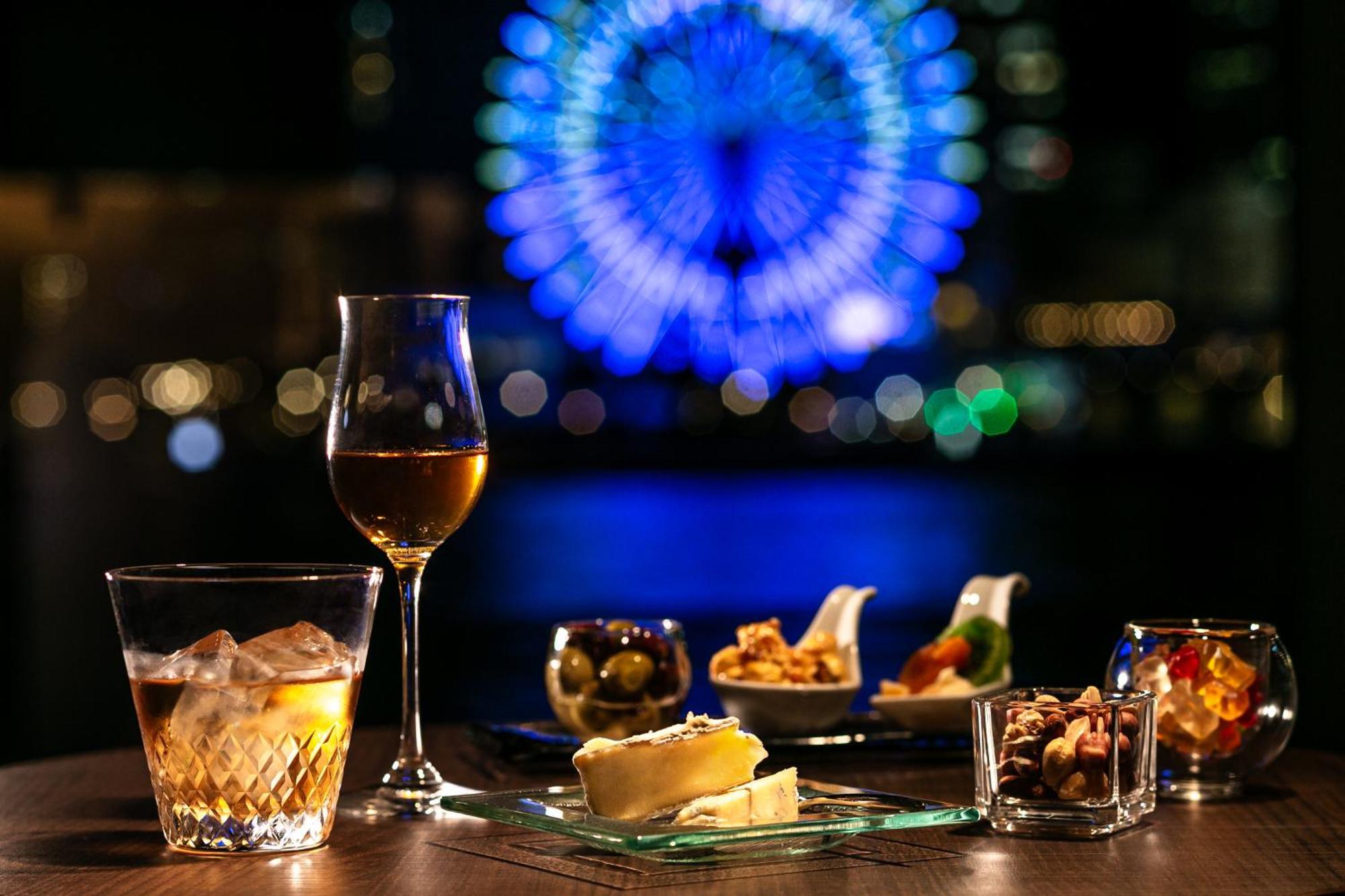 فندق كوبي ميريكين بارك أورينتال كوبه المظهر الخارجي الصورة The photo shows a dining setup with a variety of appetizers and drinks arranged on a table. In the foreground, there is a glass of clear liquid with ice and a wine glass filled with a golden beverage. A platter features several small dishes containin