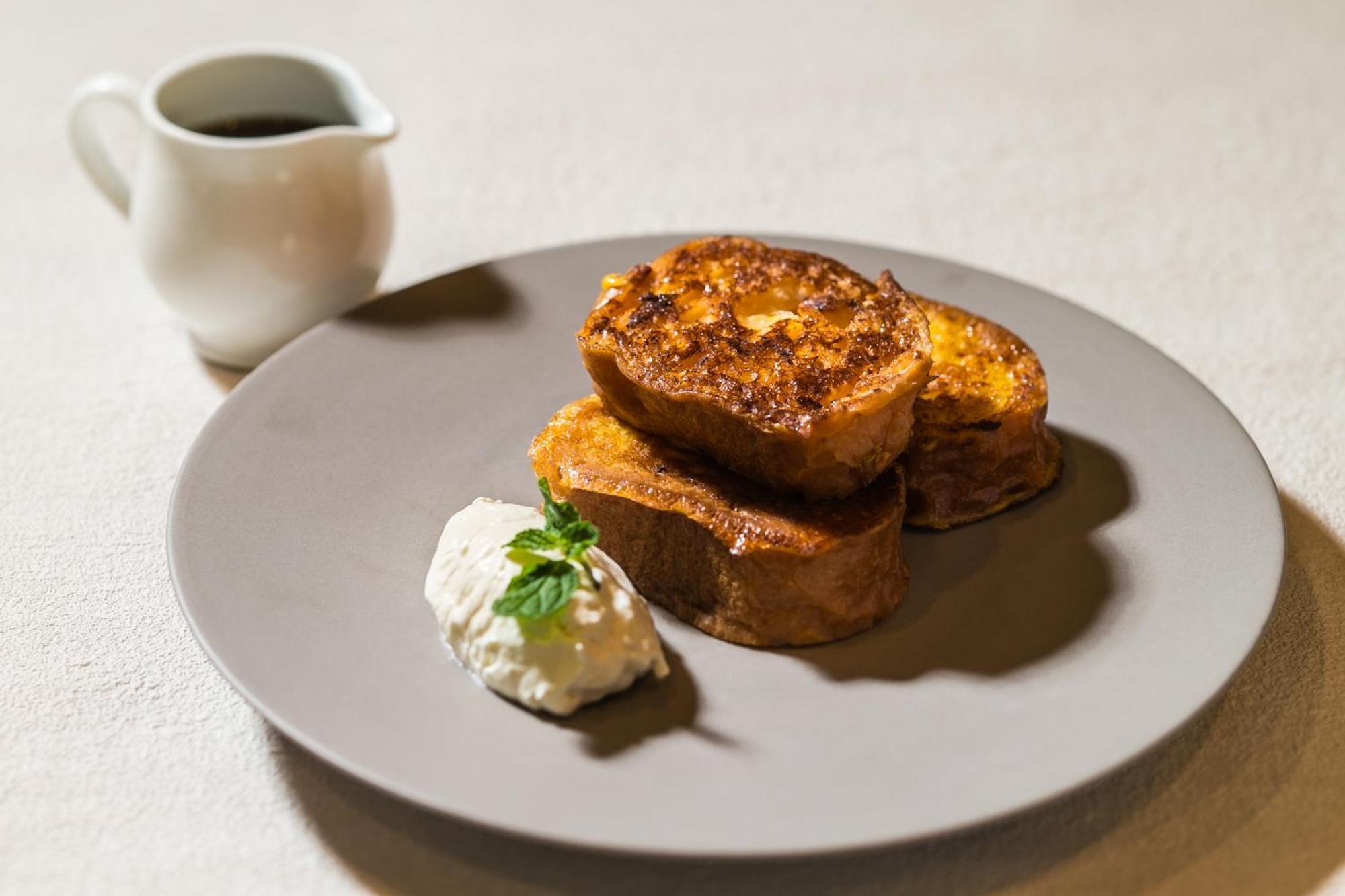 فندق كوبي ميريكين بارك أورينتال كوبه المظهر الخارجي الصورة The photo displays a plate of French toast, featuring several thick slices that are golden-brown and slightly crispy on the outside. Accompanying the toast is a dollop of whipped cream or a similar creamy topping, garnished with a small sprig of fres