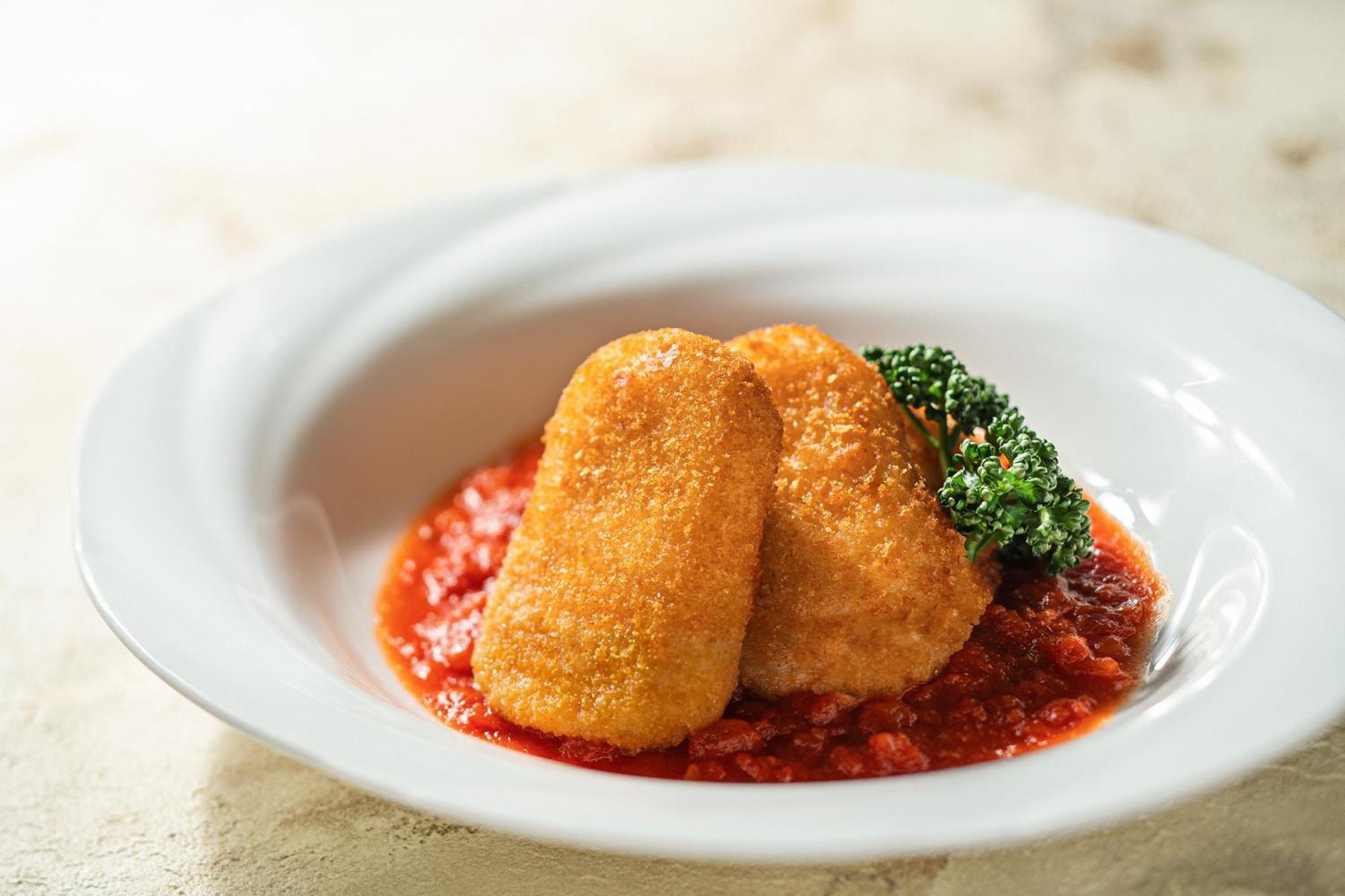 فندق كوبي ميريكين بارك أورينتال كوبه المظهر الخارجي الصورة The photo shows two breaded and fried pieces of food, likely croquettes or a similar dish, placed on a bed of rich red tomato sauce. There is a small garnish of green broccoli beside the croquettes, adding a touch of color to the presentation. The di