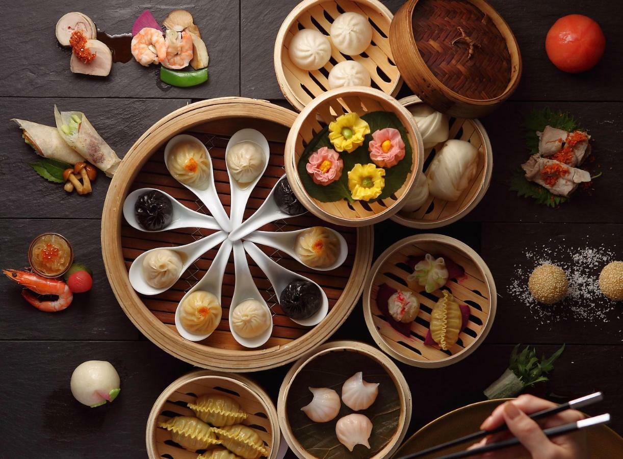 فندق كوبي ميريكين بارك أورينتال كوبه المظهر الخارجي الصورة The photo showcases a beautifully arranged assortment of dim sum and other delicacies. In the center, there is a circular bamboo steamer containing various small bowls and dishes filled with colorful dumplings, some adorned with decorative flowers. S