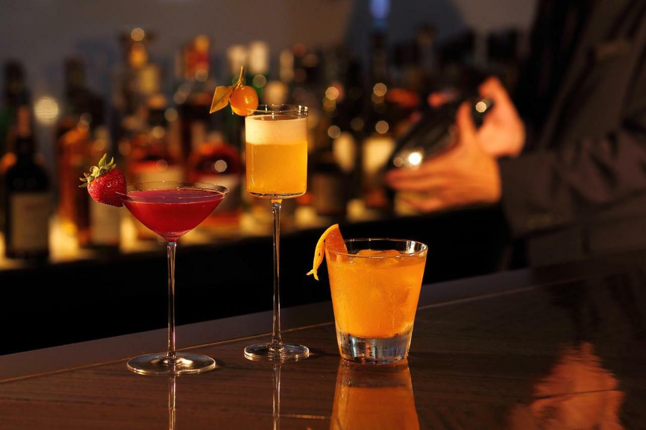 فندق كوبي ميريكين بارك أورينتال كوبه المظهر الخارجي الصورة The photo displays three cocktails arranged on a bar. 

1. **Left**: A vibrant pink cocktail served in a tall, slender glass, garnished with a fresh strawberry.
2. **Middle**: A light yellow drink in a frosted glass with a citrus twist, topped with a