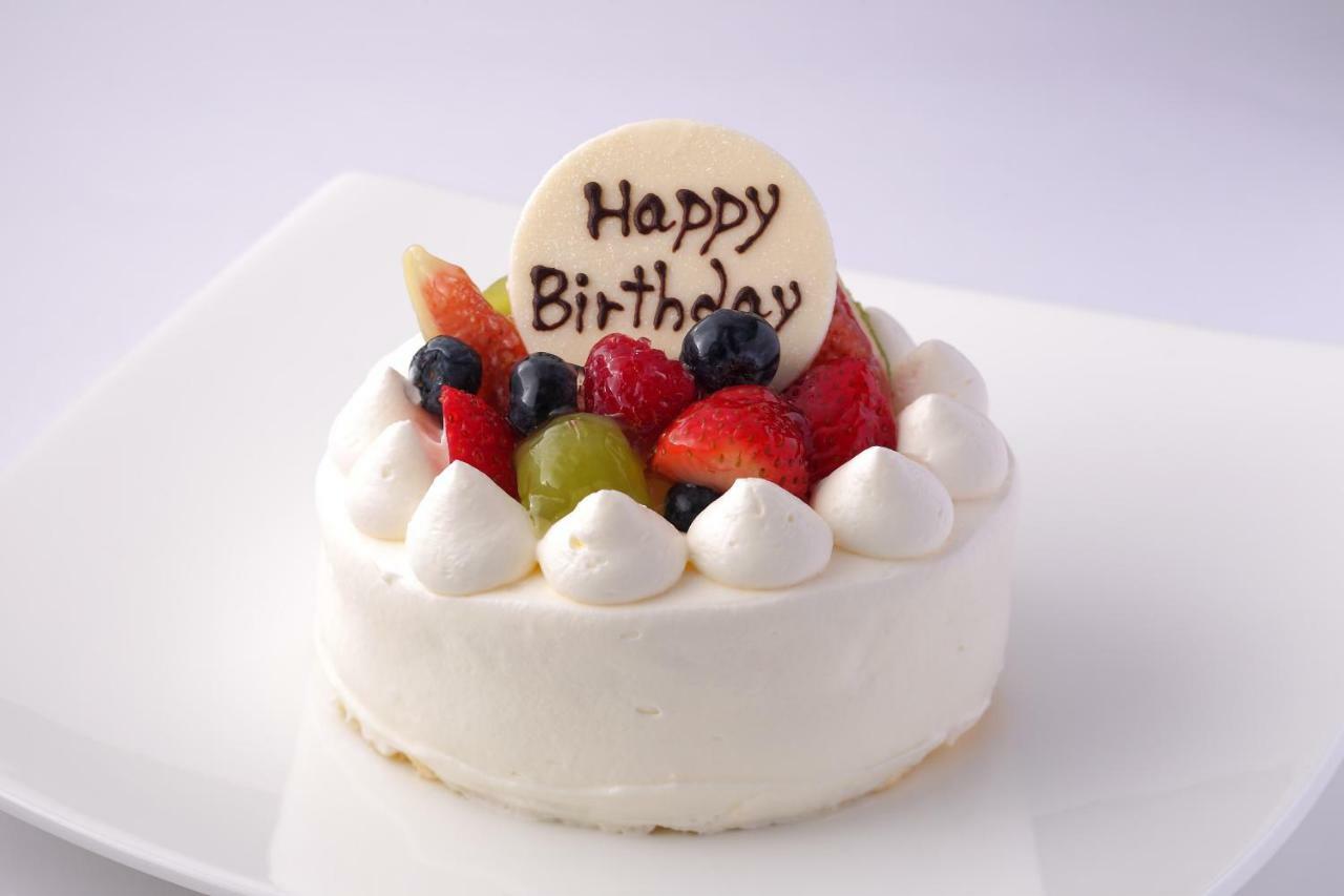 فندق كوبي ميريكين بارك أورينتال كوبه المظهر الخارجي الصورة The image shows a celebratory birthday cake. It features a round, white cake topped with an assortment of fresh fruits, including berries and slices of other fruits. At the center, there is a decorative disc that reads "Happy Birthday" in chocolate o